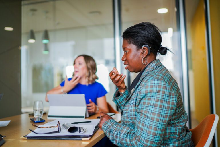 Deaf person talks to colleagues at work. Left to right: A woman with a prosthetic limb, a Deaf woman