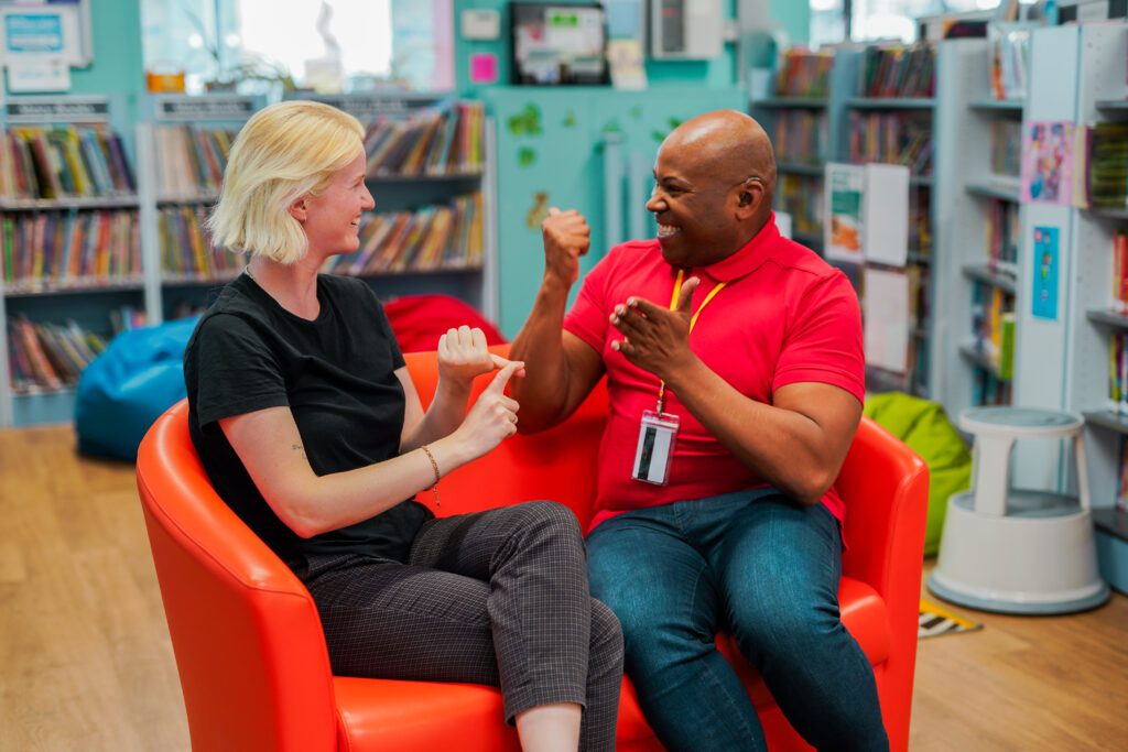 A Deaf man speaks to his friend using sign language in a library