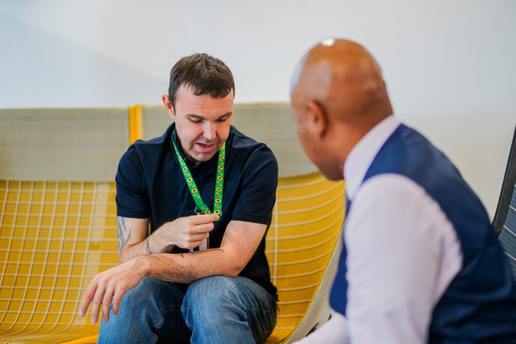 Person looks down and touches sunflower lanyard with colleague in office seating area