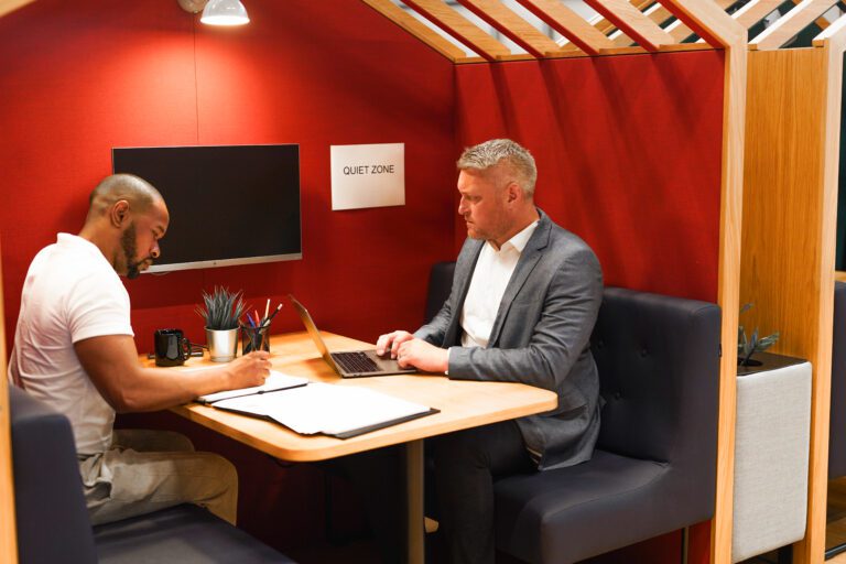 Two male colleagues work in quiet zone booth in office