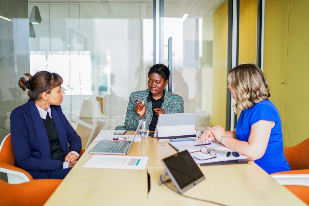 A group of people with diverse disabilities in a work meeting. Left to right: A woman with a mental health condition, a woman with hearing loss and a woman with a prosthetic limb