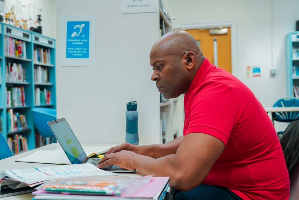 A Deaf man using a laptop in a library