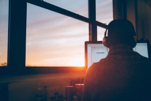 Person sitting facing monitor while sun setting in the distance