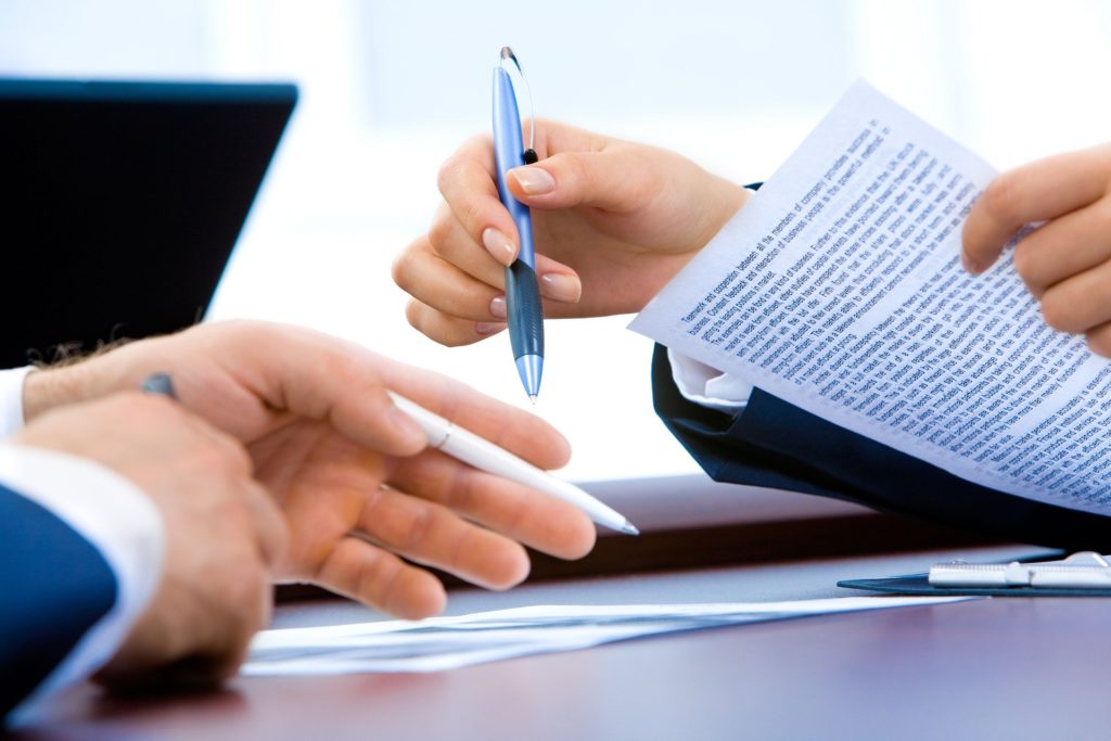 Two people in a meeting. Hands are shown to hold pens and documents