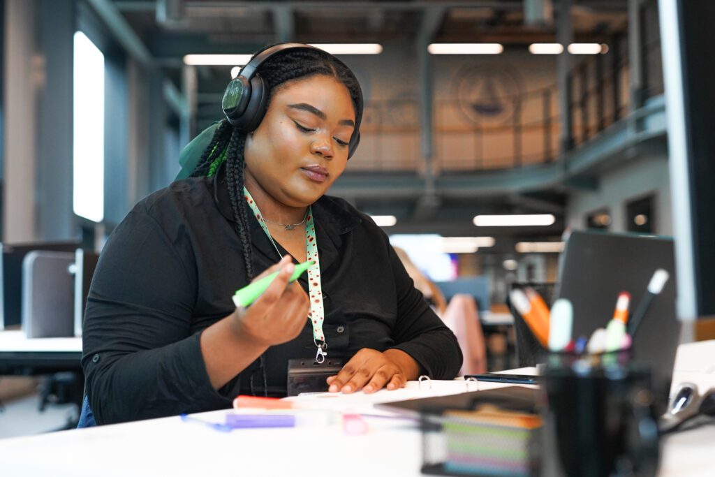 Person with less-visible disabilities at desk highlights paperwork wearing noise cancelling headphones