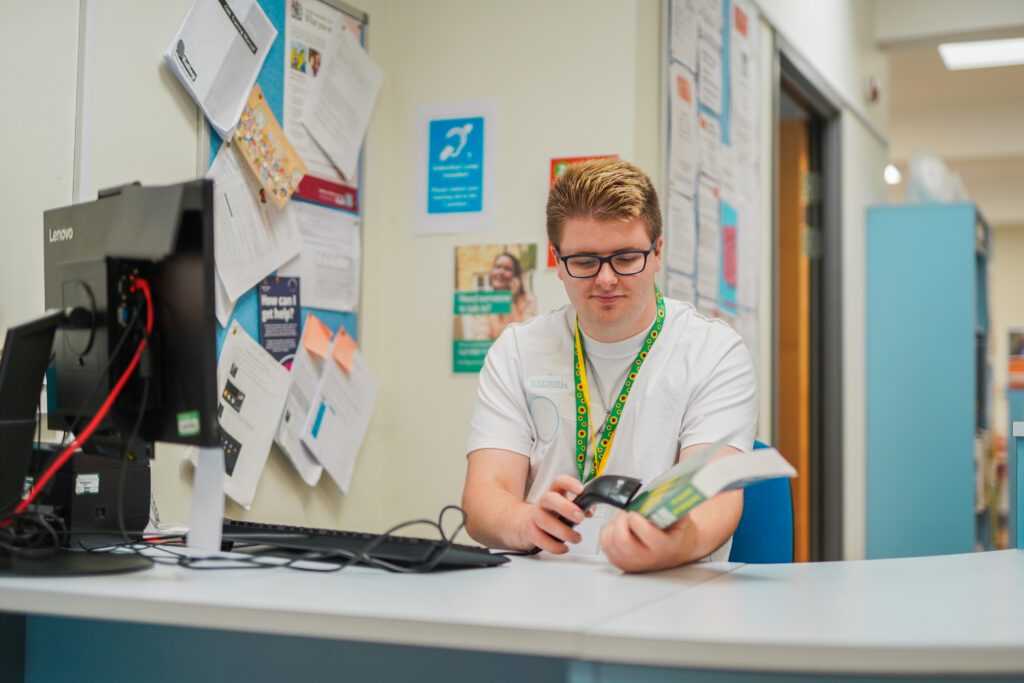 Employee with autism scanning a book at a computer at desk in library