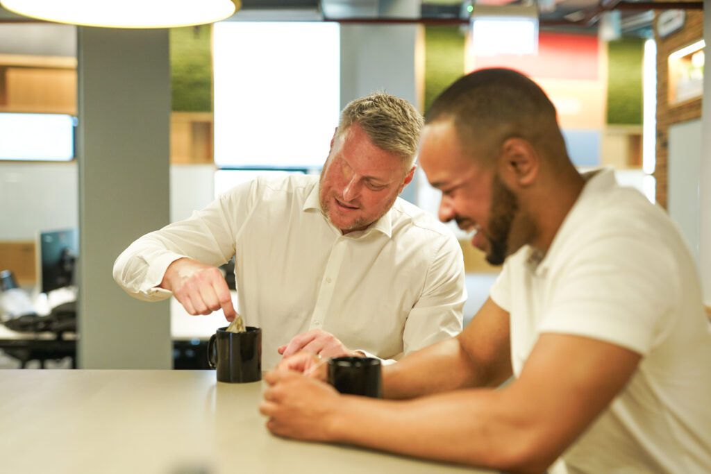 Person with facial difference and sight loss laughs with colleague while making cup of tea