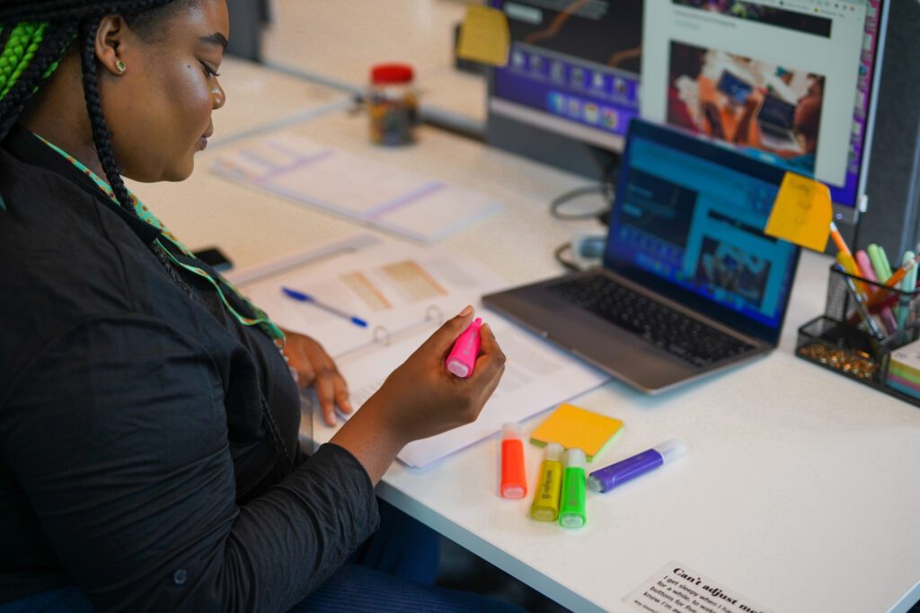 Woman with dyslexia and other less-visible disabilities uses a highlighter while sitting at a desk in front of screens