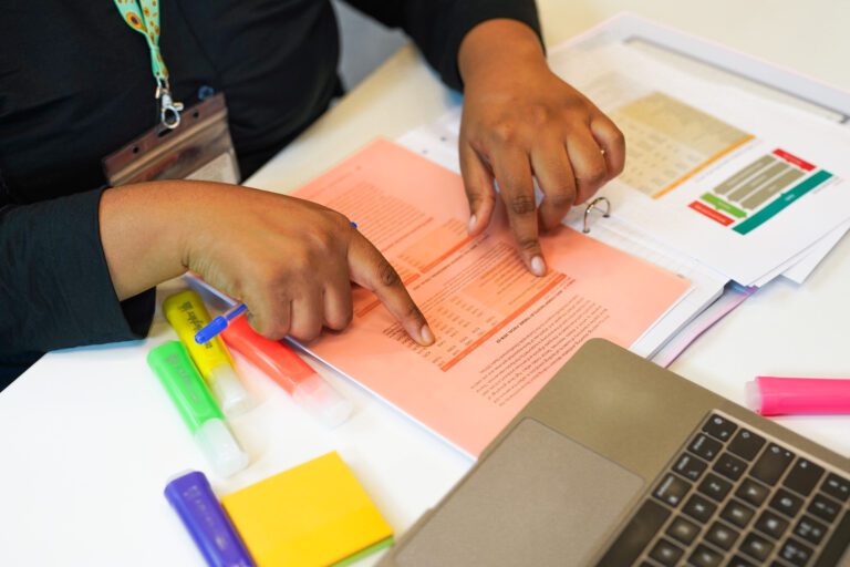 Person wearing a sunflower lanyard to show less-visible disabilities reads worksheets using tinted coloured overlay to aid reading