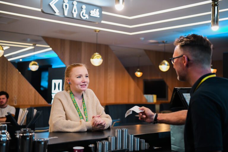 Woman with less visible disabilities is served at the cinema. She is wearing a sunflower lanyard to show she has less-visible disabilities