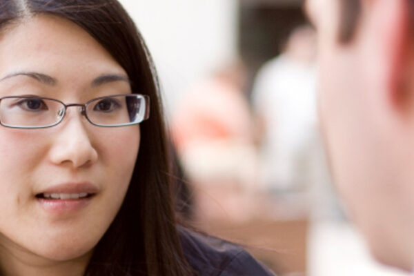 Asian woman with glasses speaking to another person off camera