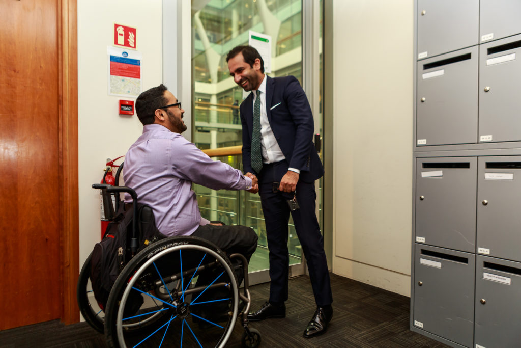 Wheelchair user shaking hands with another professional in the lobby of an office.