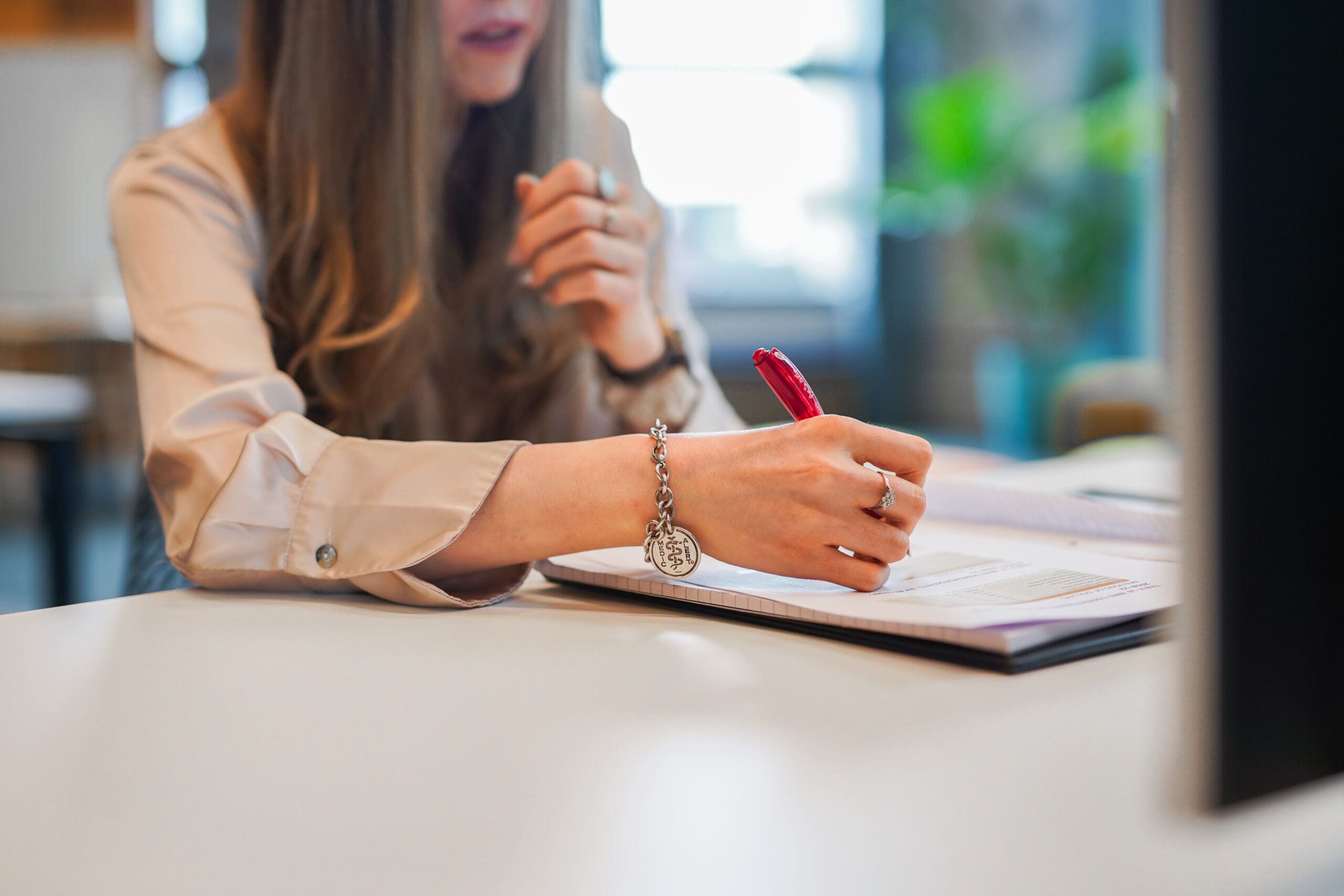 Person wearing medical information bracelet writes notes at desk.