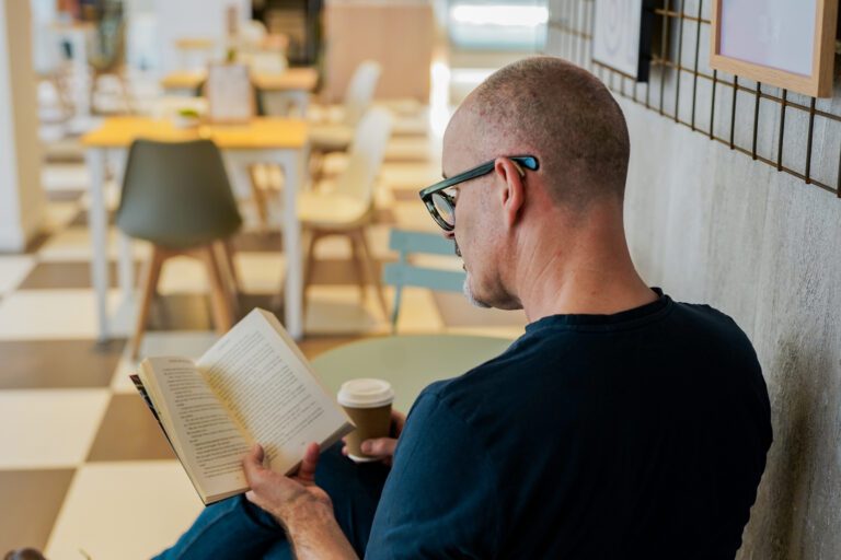 A Deaf man wearing hearing aids has a coffee while reading a book in a cafe