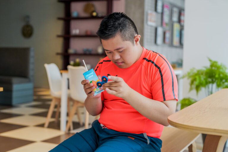 A man with Down's Syndrome uses a fidget spinner and drinks juice in a cafe