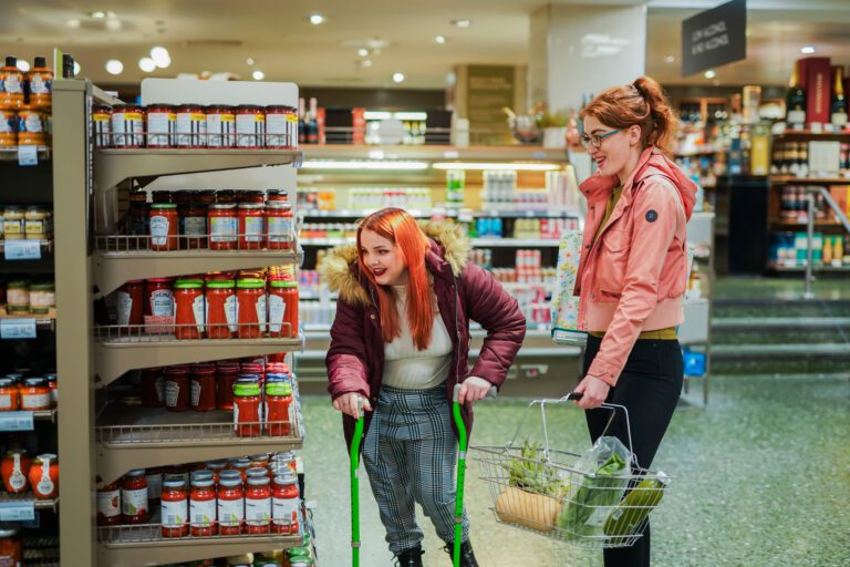 Person using walking sticks shops in a supermarket with a friend