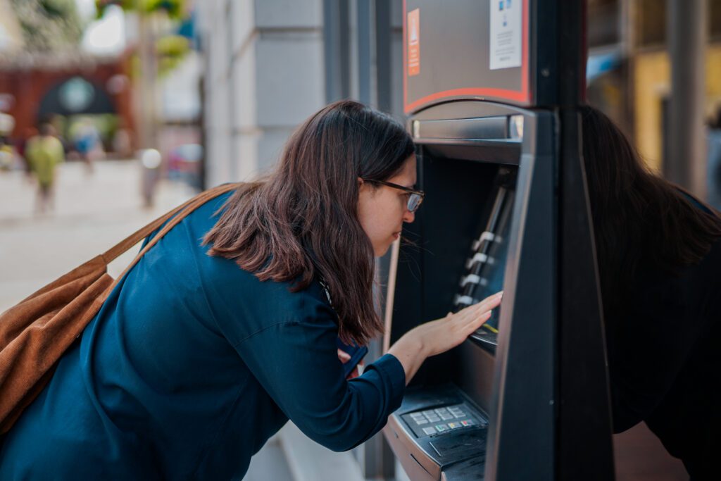 A woman with a less visible disability (visual impairment) who wears glasses uses a cash machine.