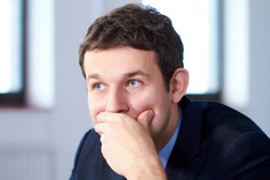 A photo of a man looking to the side with his hand over his mouth in thought.