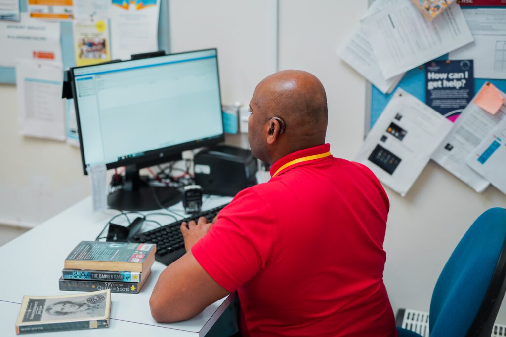 A Deaf man using hearing aids working at a library enquiry desk