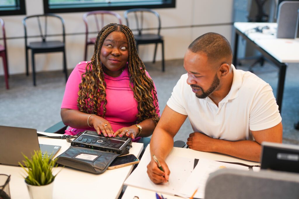 A blind woman works on a braille note next to a colleague