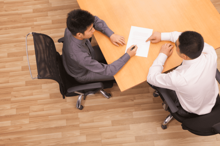 Two colleagues in a meeting signing paperwork at a desk