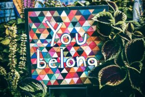 A colourful paper sign with the words "You belong" in collage, surrounded by lush plants.