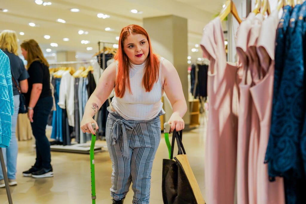 Woman with Cerebral Palsy uses walking sticks while shopping for clothes in a store.