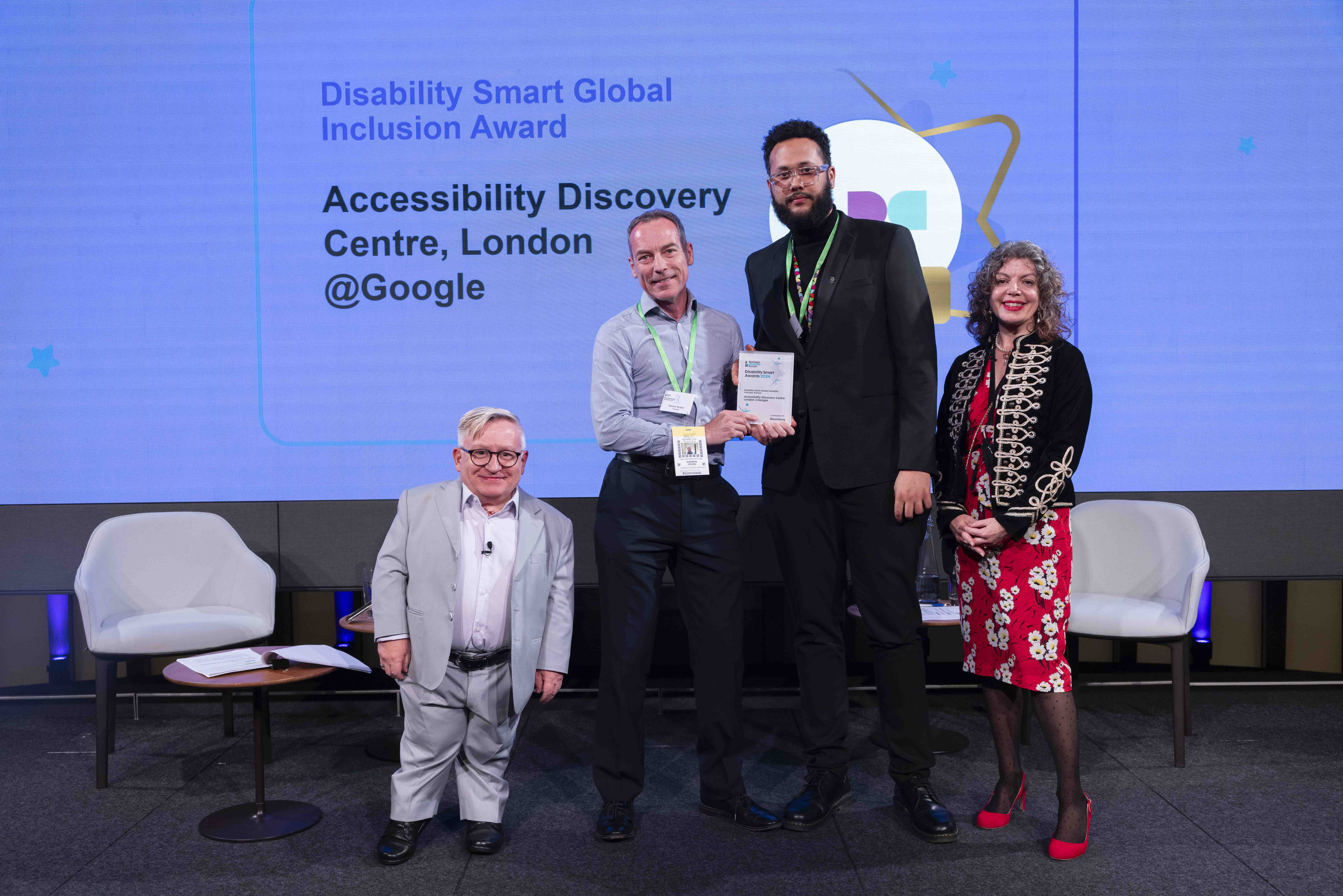 The Google team posing with their award on stage with co-hosts Diane Lightfoot and Simon Minty at the Disability Smart Awards 2024 ceremony.