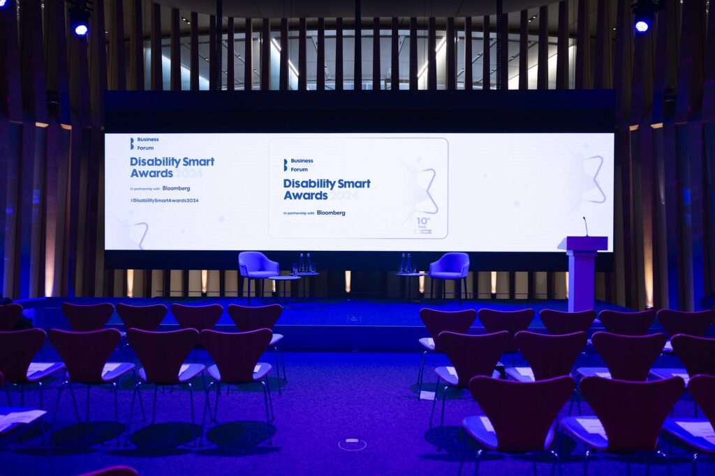 The empty auditorium of the Disability Smart Awards 2024 ceremony, photographed from the back of the room. The event logo is projected onto a big screen above the stage.