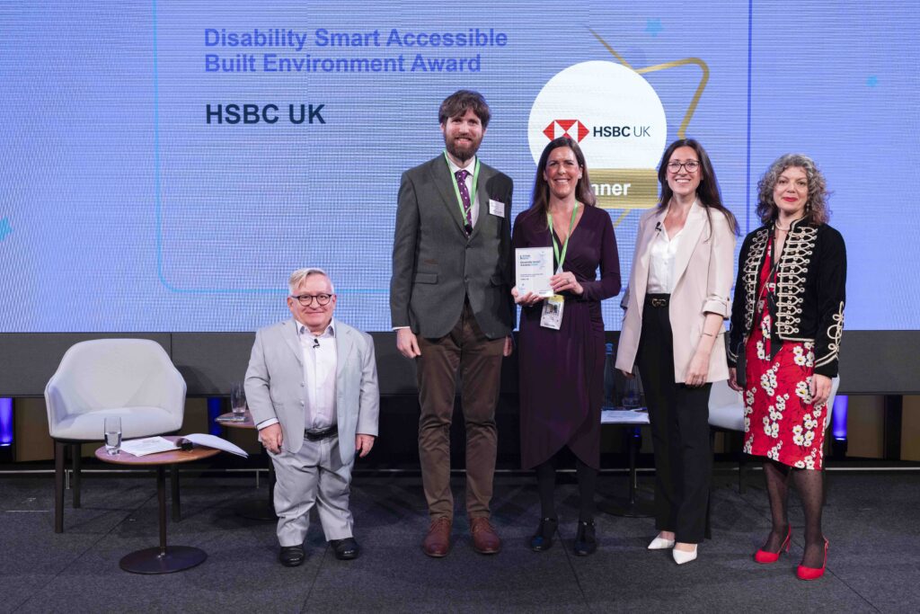 The HSBC team posing with their award on stage with co-hosts Diane Lightfoot and Simon Minty at the Disability Smart Awards 2024 ceremony.