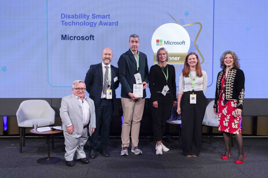 The Microsoft team posing with their award on stage with co-hosts Diane Lightfoot and Simon Minty at the Disability Smart Awards 2024 ceremony.