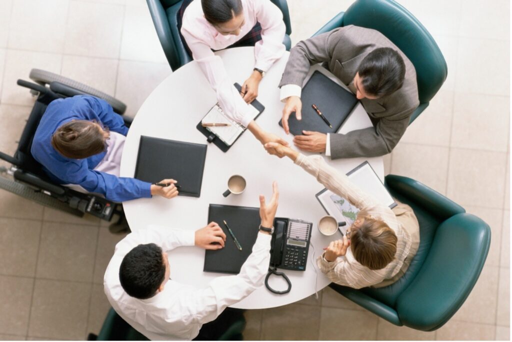 Above view of a meeting at a table, where two people are shaking hands across the table