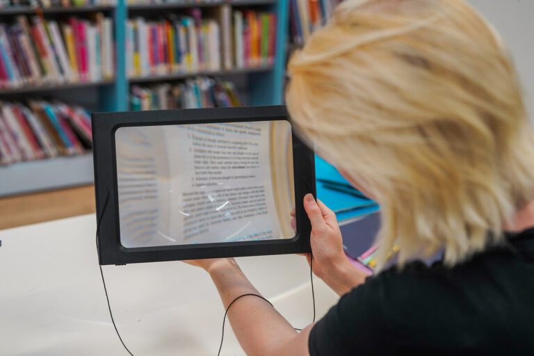 Person with sight loss holds an assistive reader magnifying glass