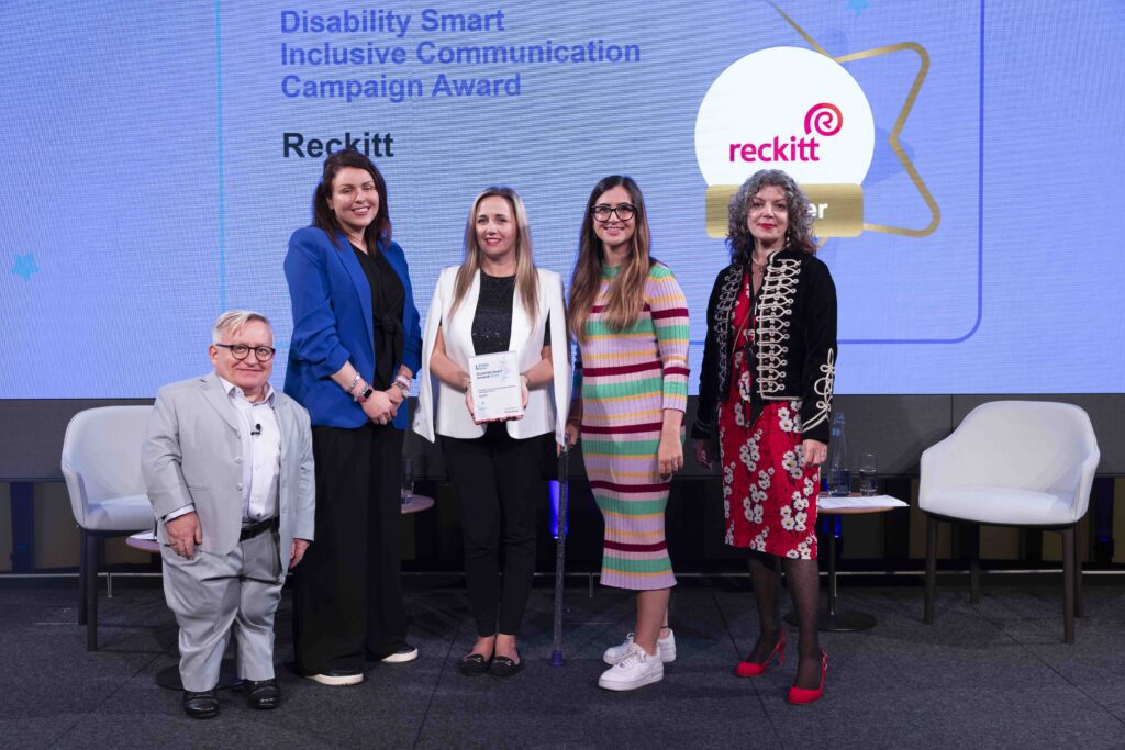 The Reckitt team posing with their award on stage with co-hosts Diane Lightfoot and Simon Minty at the Disability Smart Awards 2024 ceremony.