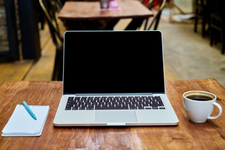 A desk with a laptop, a notepad and pen, and a coffee mug.