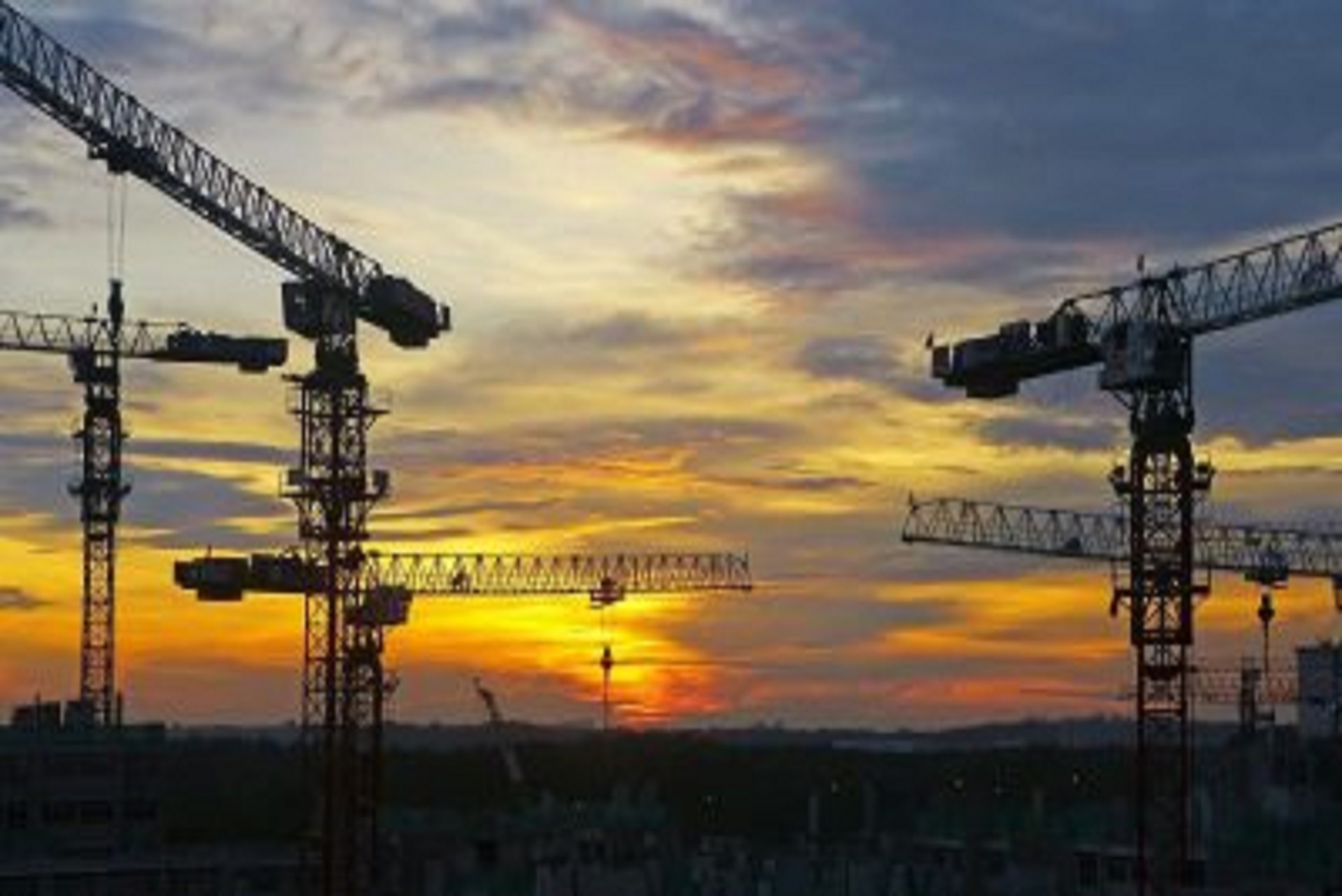 Construction cranes against a sunset.