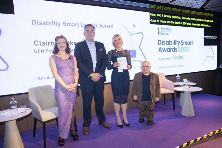 Claire Cookson posing with her award on stage at the Disability Smart Awards 2023 ceremony.