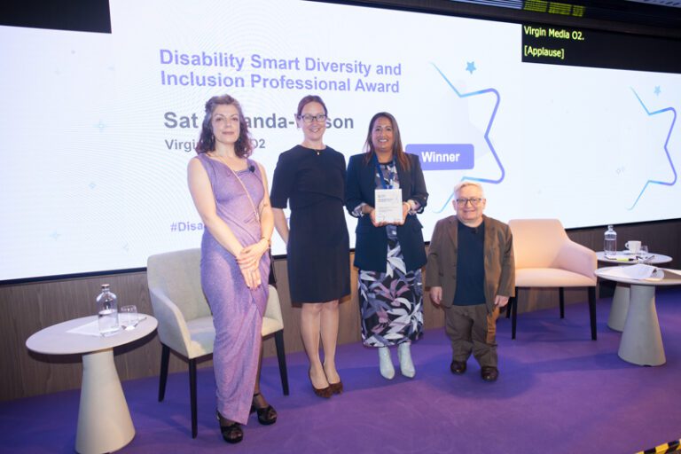 Sat Jabanda-Wilson posing with their award on stage at the Disability Smart Awards 2023 ceremony.