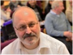 Headshot of Graeme Whippy, a white man with glasses and a beard. In the photo he is sitting in the audience at a conference.