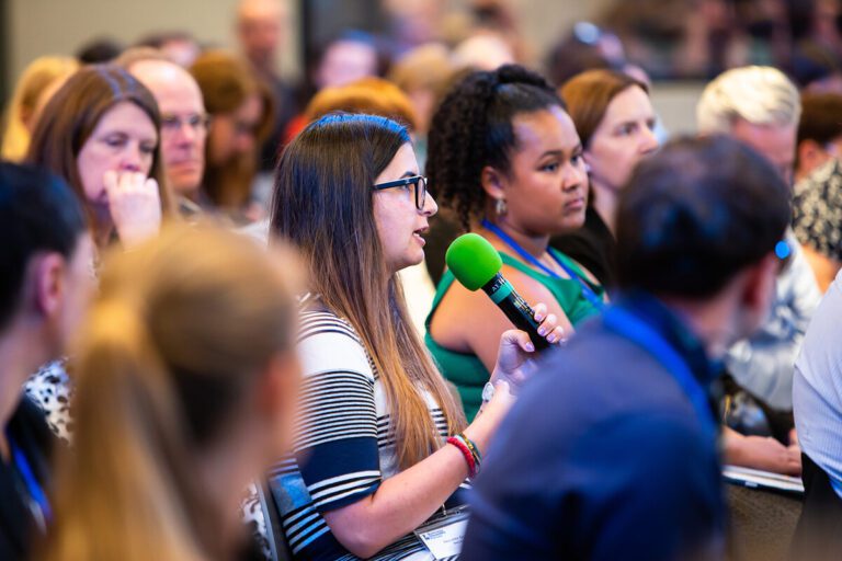 Close up on an audience member asking a question into a microphone at an event.