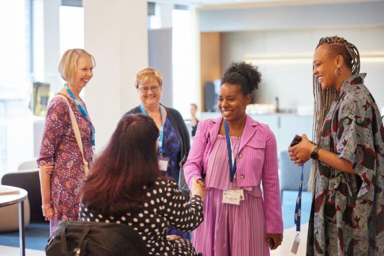 2 delegates, including a wheelchair user, shaking hands at an event. 3 other guests look on, all smiles.