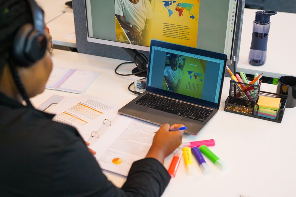 Person with a less-visible disability working at a desk. They are using noise-cancelling headphones and highlighters.