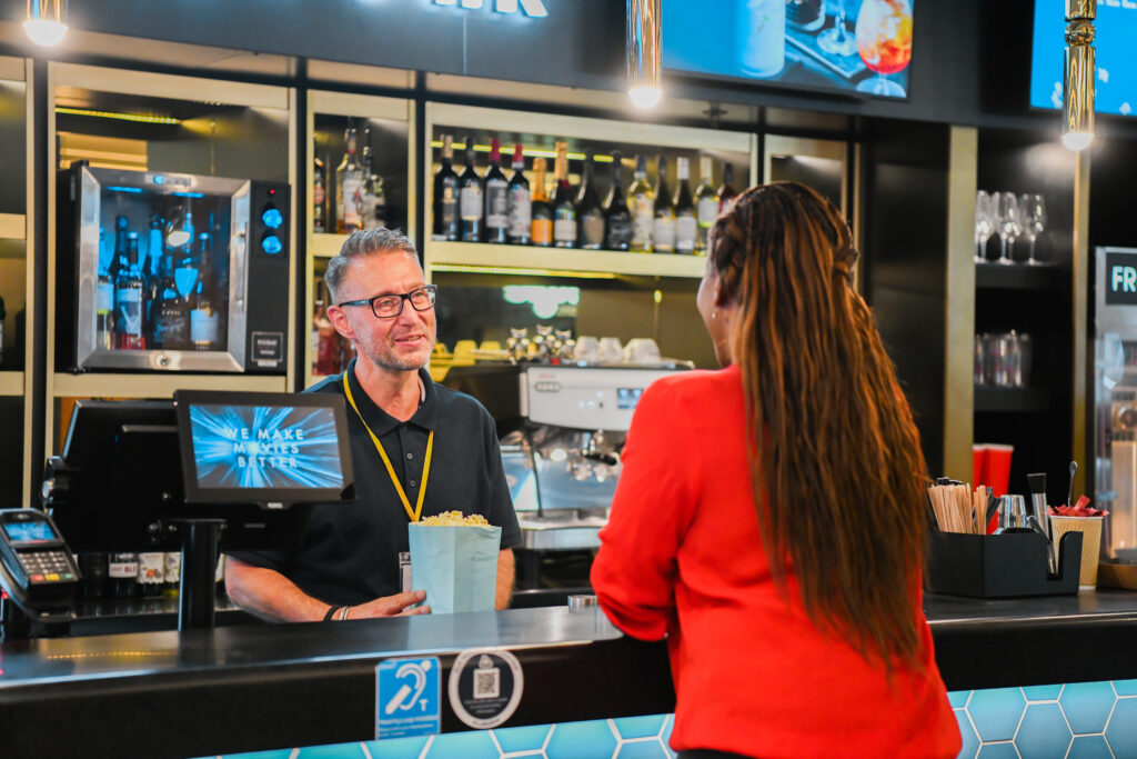 Sales assistant with less-visible disability serves popcorn to customer at cinema