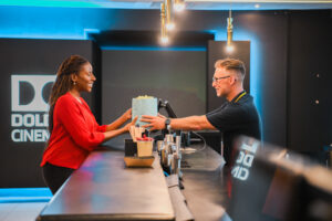 Sales assistant with less-visible disability passes popcorn to customer at cinema.