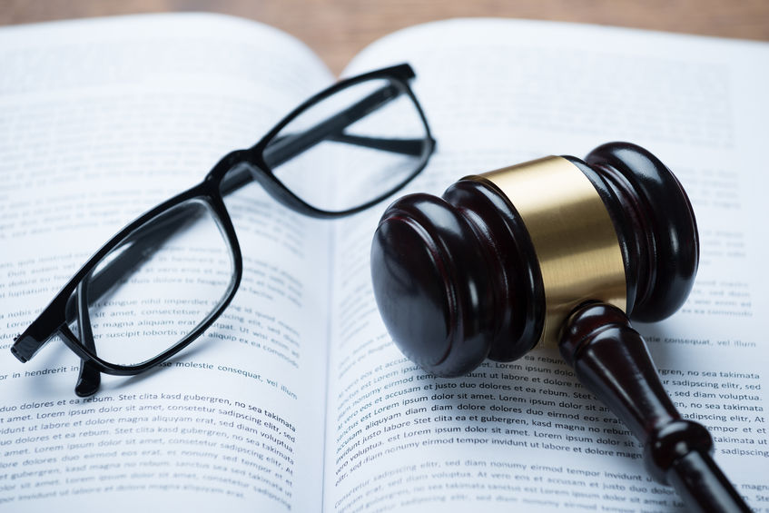 A pair of glasses and a gavel laid on an open law book.