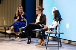 3 speakers sitting in chairs on stage at a conference.