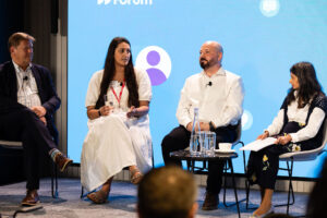 4 speakers sitting in chairs on stage at a conference.