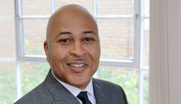 Headshot of Courtney Swaby, a smiling Black man in a grey business suit.