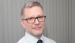 Headshot of Keith Harris,  a white man with short white hair and glasses wearing a shirt and tie.