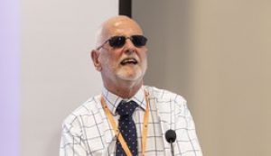 Headshot of Rick Williams, a white man wearing black glasses. In the photo he is speaking onstage at an event.